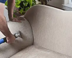Professional upholstery cleaner deep-cleaning a fabric sofa with a handheld extraction tool and hose in Fresno, CA.